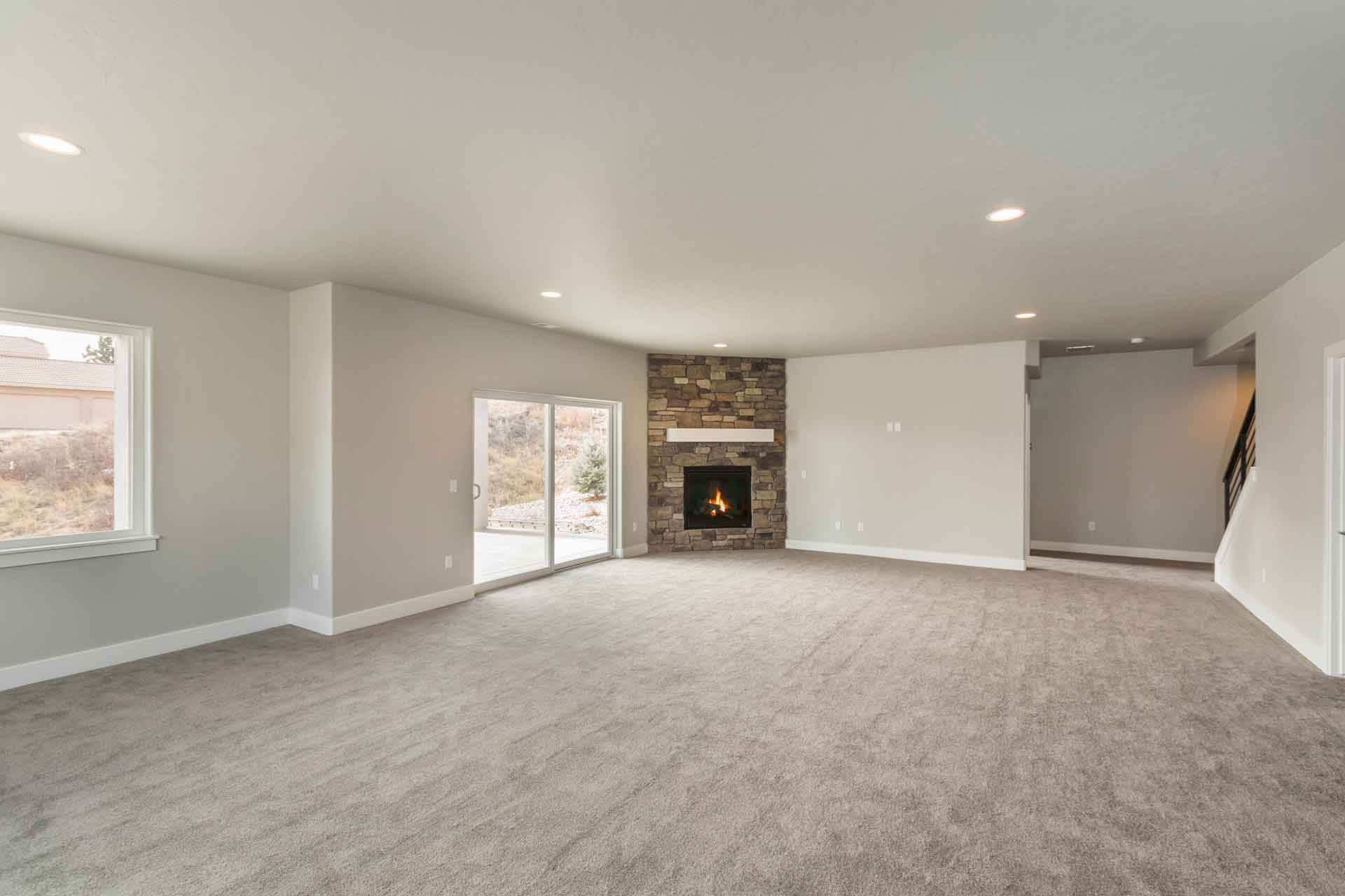 An empty basement with tan carpeting, grey walls and a fireplace