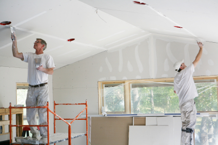 Two men on ladders installing drywall on a ceiling