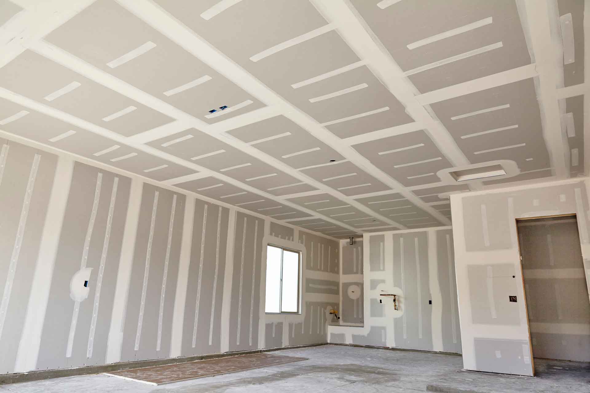 A large room with newly-installed drywall, not yet painted