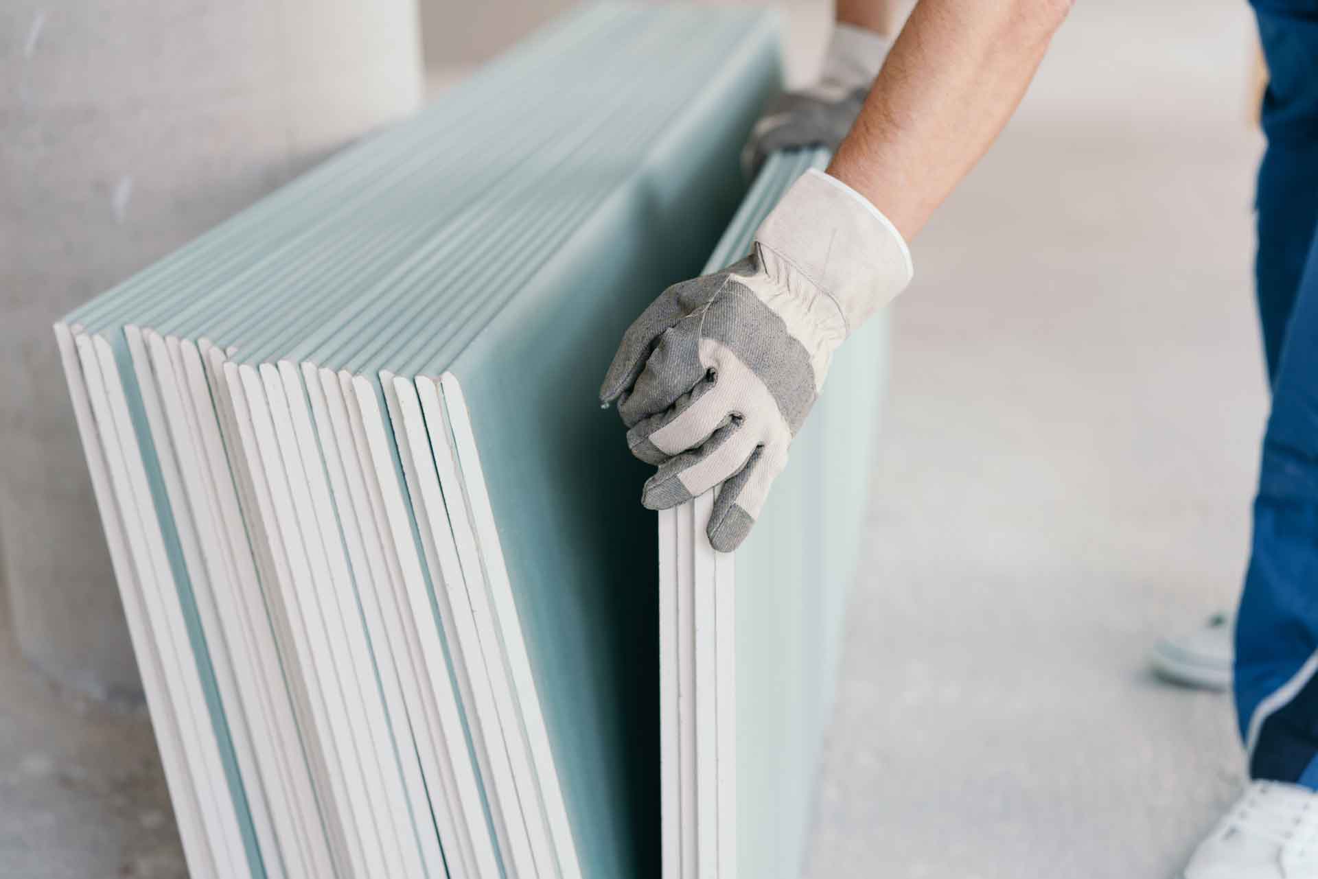 Gloved hands moving several sheets of drywall